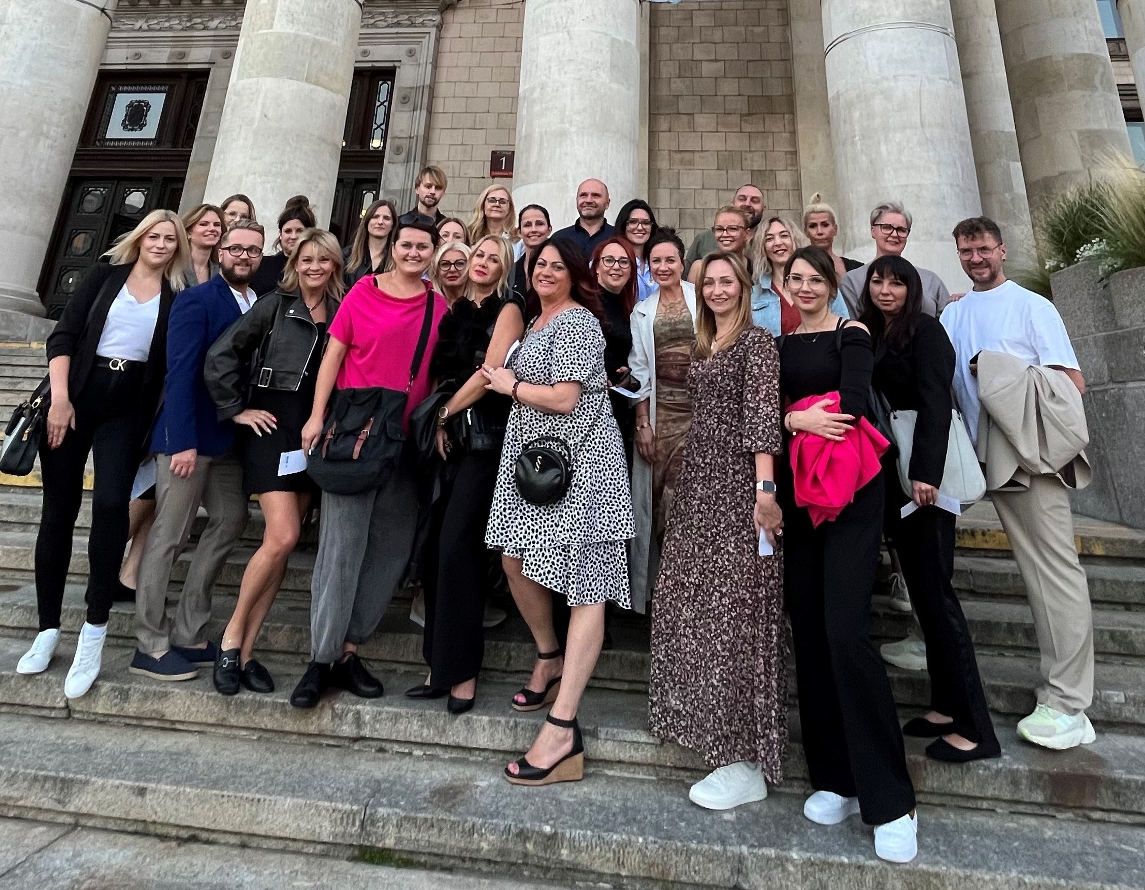 Grupa ludzi stojących na schodach przed dużym budynkiem