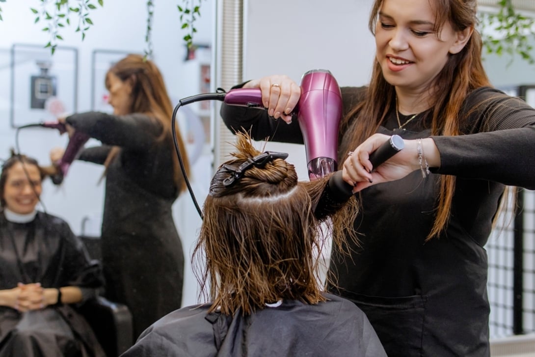 Fryzjerka susząca klientce włosy suszarką w salonie fryzjerskim