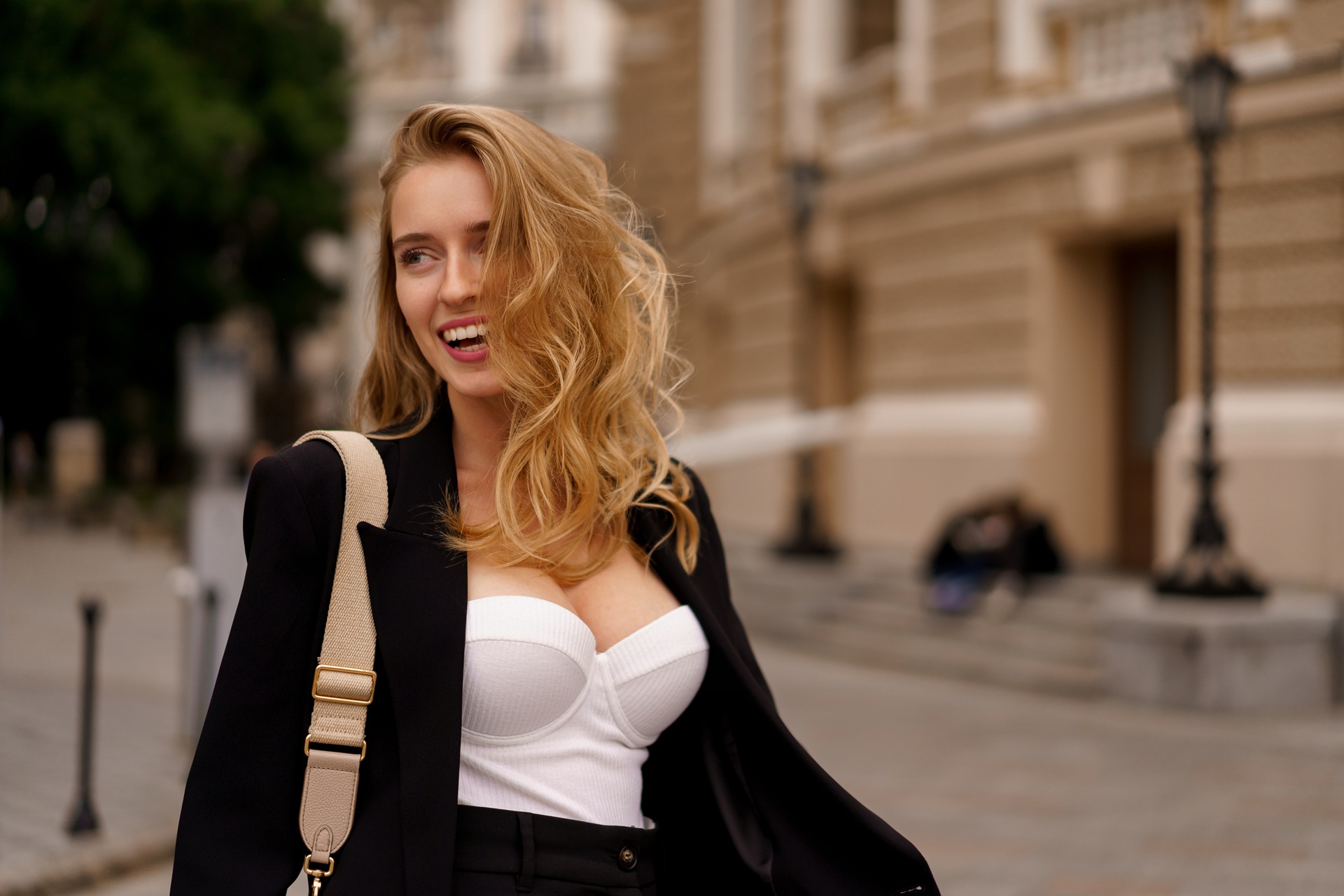 Uśmiechnięta młoda kobieta z falowanymi blond włosami, idąc przez miasto