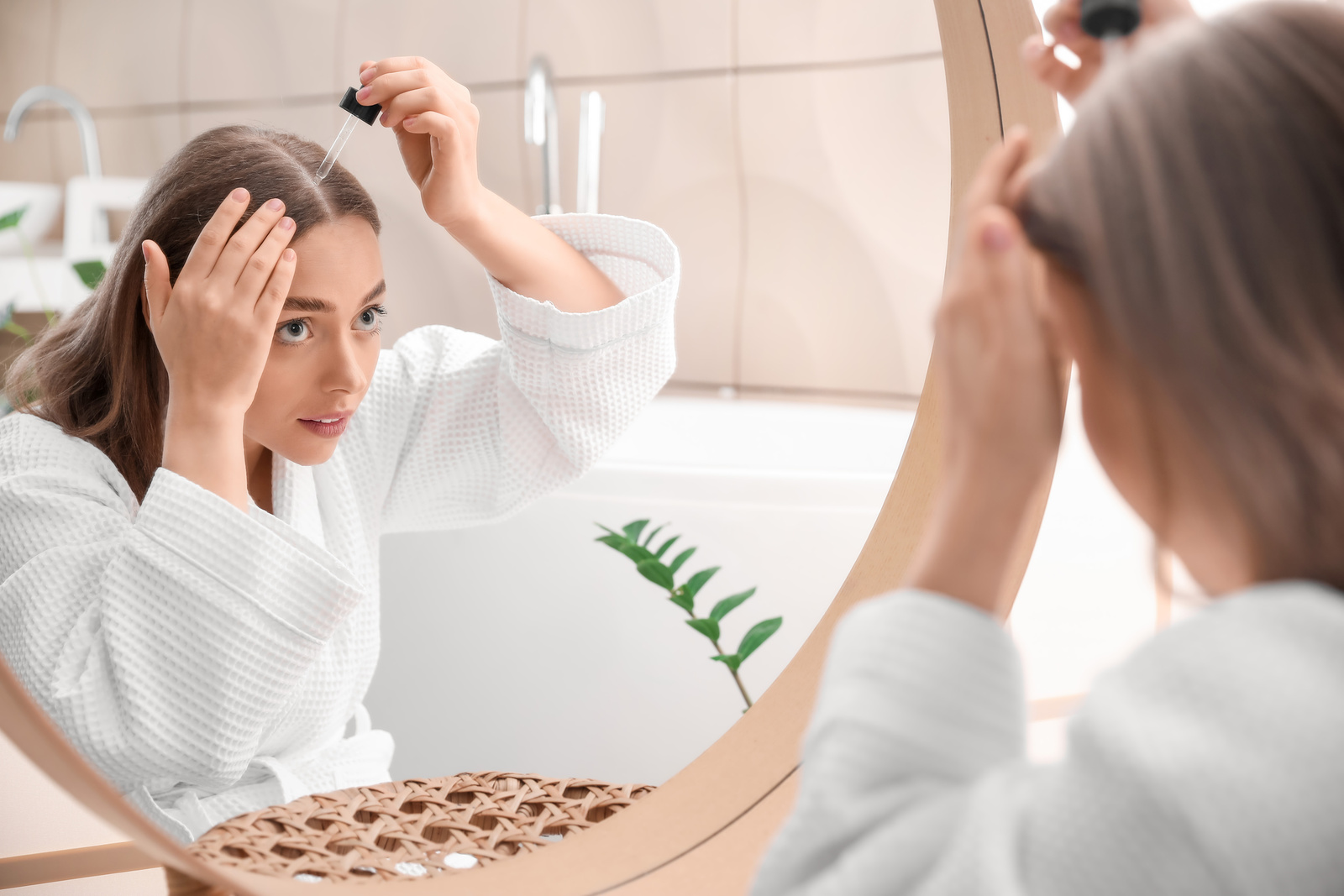 Młoda kobieta przed lustrem nakłada serum na skórę głowy